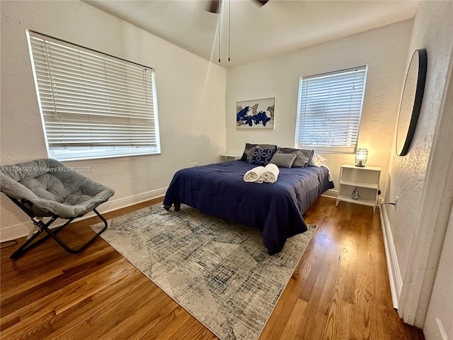 bedroom with ceiling fan, a textured wall, baseboards, and wood finished floors