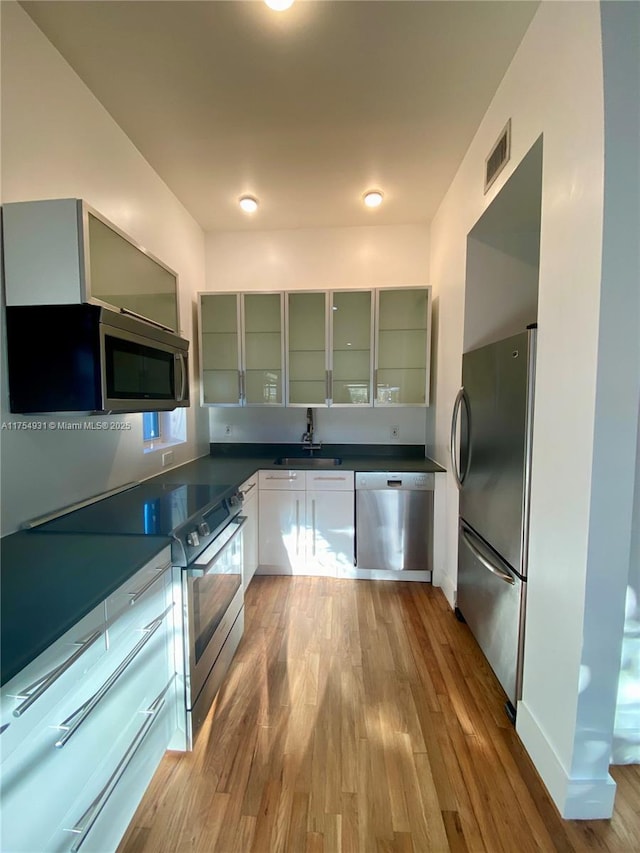 kitchen featuring visible vents, dark countertops, appliances with stainless steel finishes, wood finished floors, and a sink