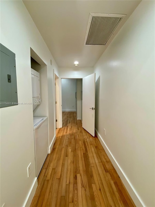 hallway with stacked washer and dryer, electric panel, visible vents, baseboards, and light wood-style flooring