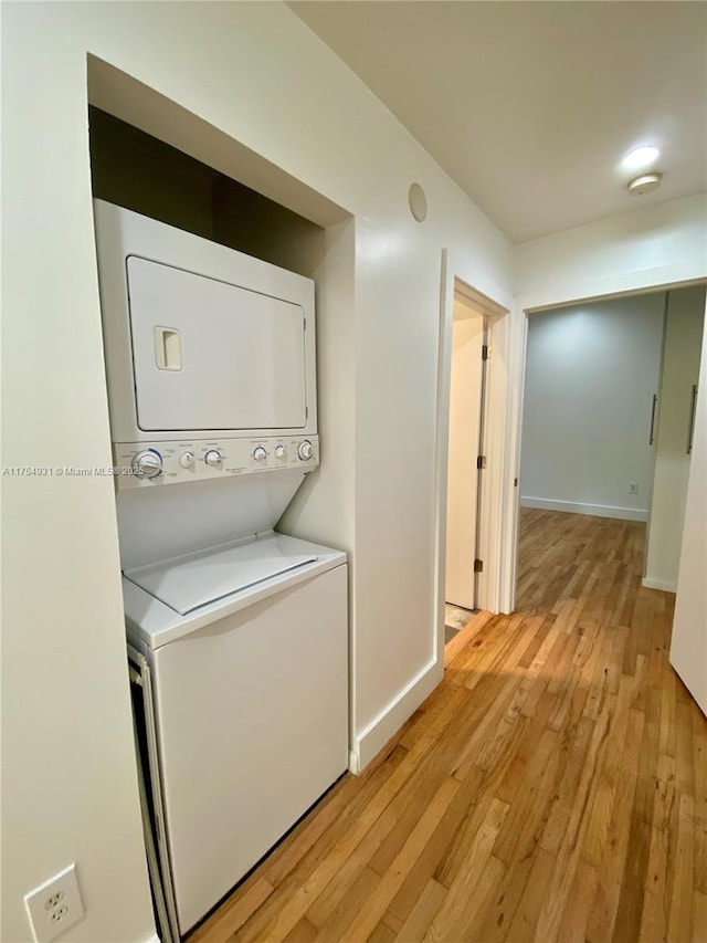 washroom with laundry area, light wood finished floors, stacked washing maching and dryer, and baseboards