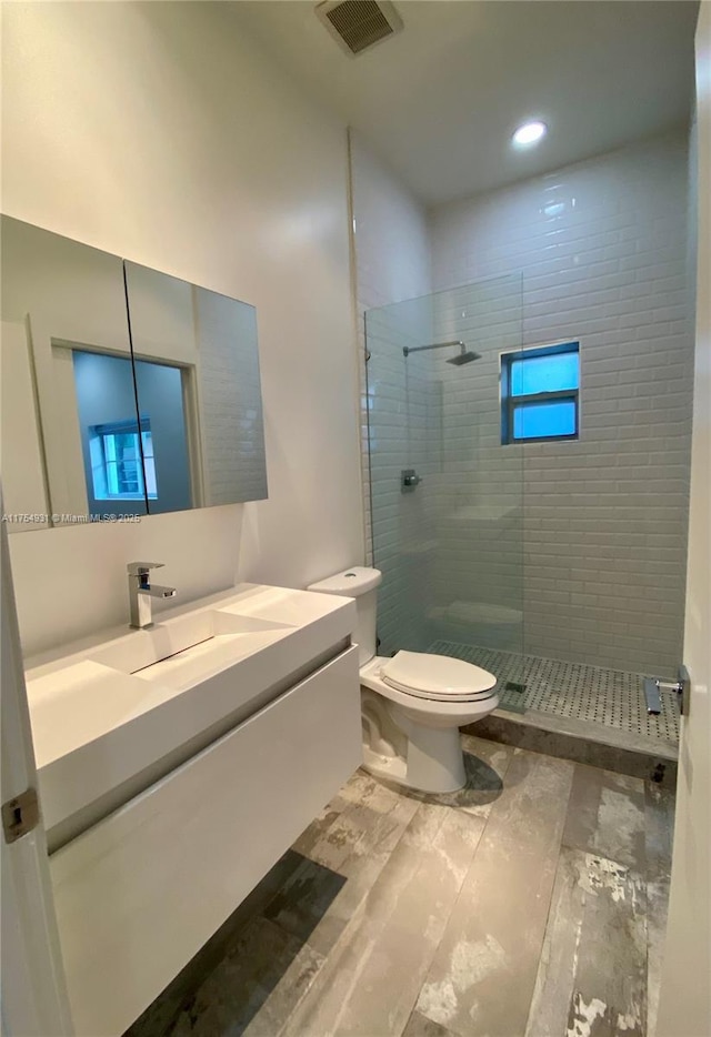 full bathroom featuring toilet, vanity, a walk in shower, and visible vents