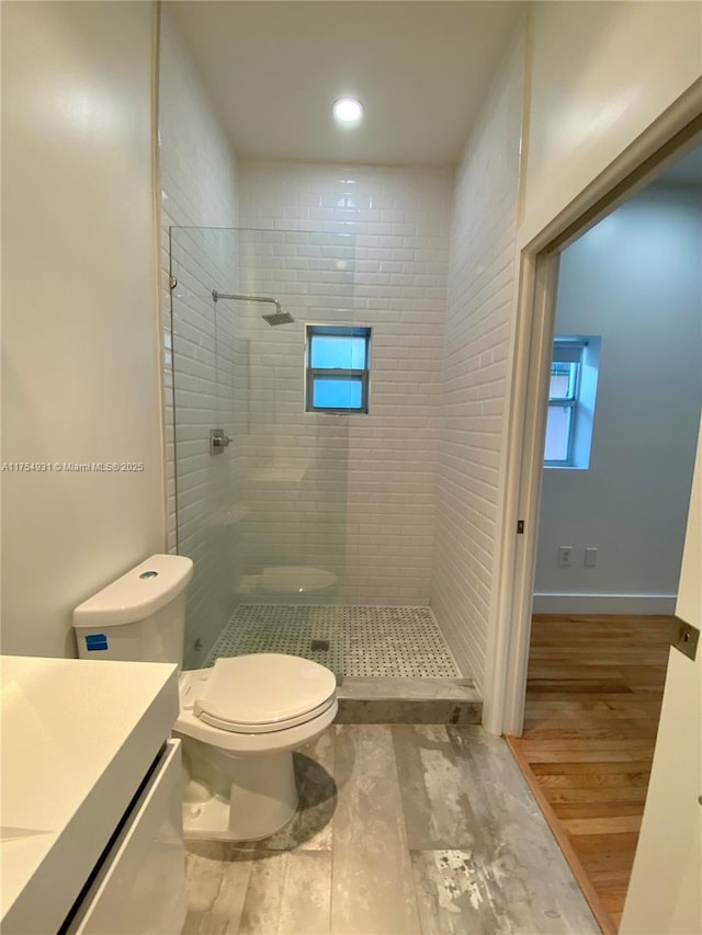 full bathroom with baseboards, toilet, wood finished floors, a tile shower, and vanity