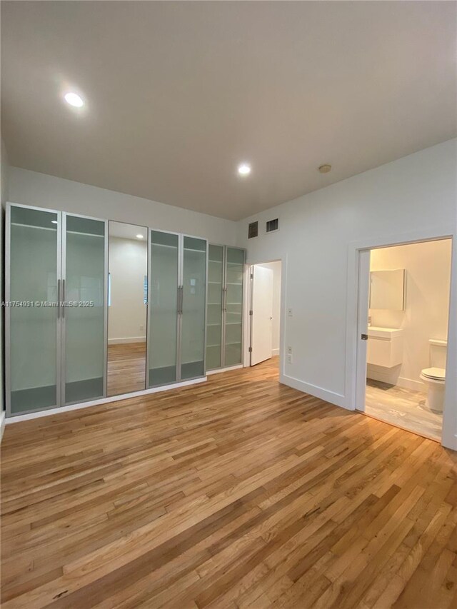 unfurnished bedroom featuring ensuite bath, wood finished floors, two closets, and recessed lighting