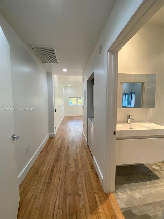 hall featuring a sink, wood finished floors, visible vents, and baseboards