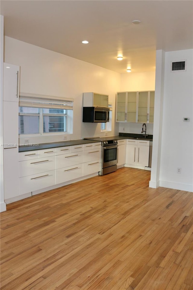 kitchen featuring stainless steel appliances, dark countertops, visible vents, light wood-style floors, and glass insert cabinets