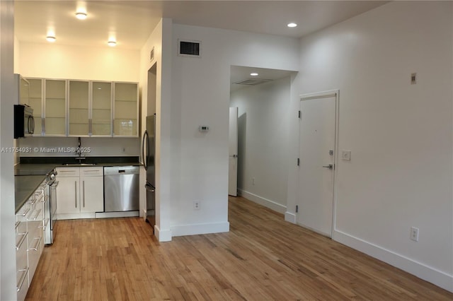 kitchen featuring stainless steel appliances, a sink, baseboards, light wood finished floors, and dark countertops