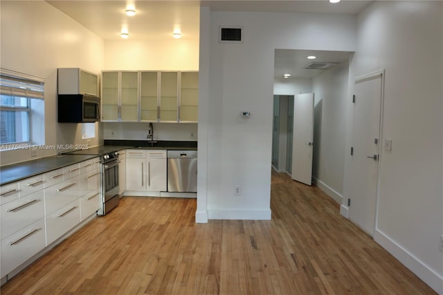 kitchen with stainless steel appliances, dark countertops, visible vents, light wood-style flooring, and a sink