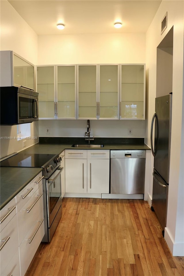 kitchen with dark countertops, light wood finished floors, appliances with stainless steel finishes, and a sink