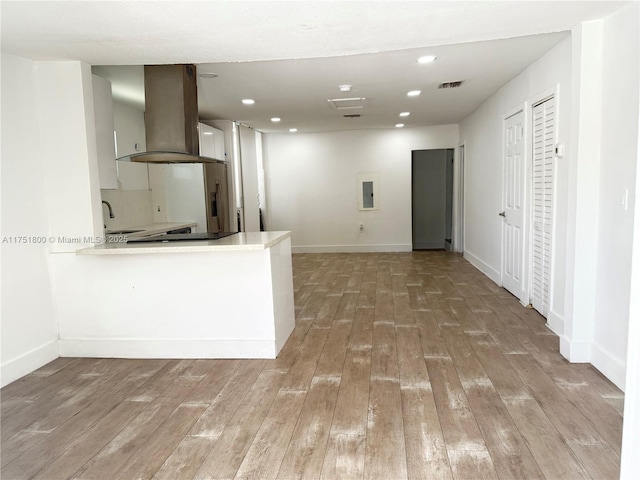 kitchen with visible vents, island range hood, a peninsula, light wood-style floors, and a sink