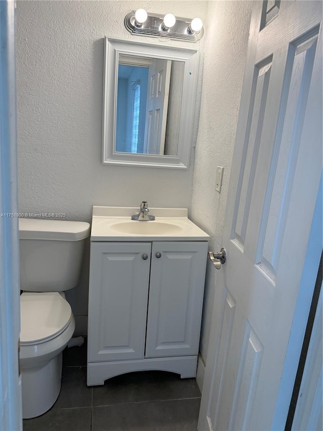 bathroom with toilet, a textured wall, vanity, and tile patterned floors