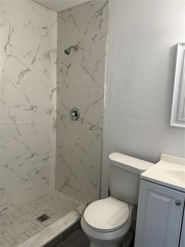 bathroom featuring a stall shower, a textured wall, vanity, and toilet