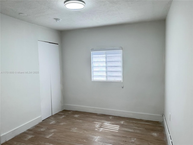 unfurnished bedroom with a textured ceiling, a closet, wood finished floors, and baseboards