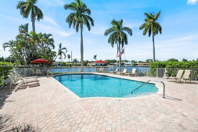 community pool featuring a water view, fence, and a patio