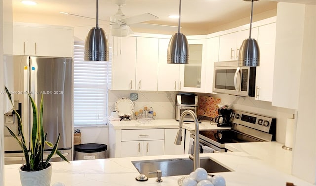 kitchen with white cabinets, decorative backsplash, glass insert cabinets, light stone counters, and stainless steel appliances