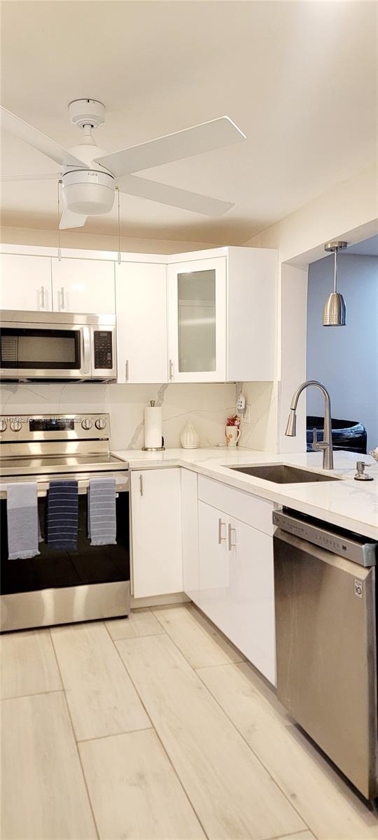 kitchen with stainless steel appliances, light countertops, white cabinetry, and a sink