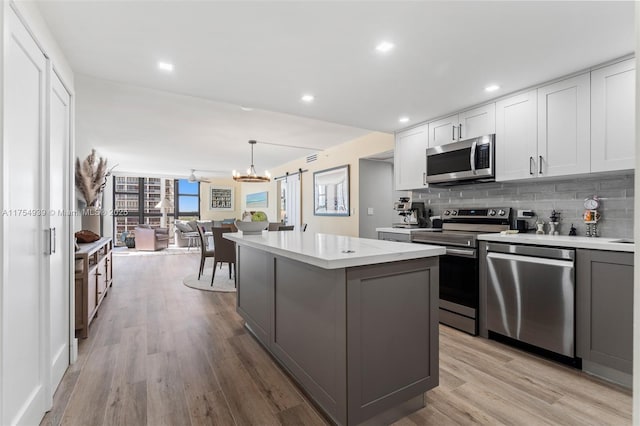 kitchen featuring light wood finished floors, stainless steel appliances, backsplash, and light countertops