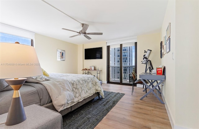 bedroom with baseboards, a ceiling fan, access to outside, expansive windows, and light wood-type flooring