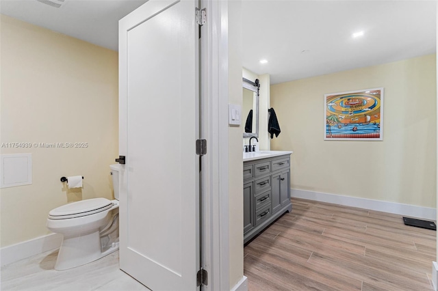 bathroom with toilet, baseboards, wood finished floors, and vanity