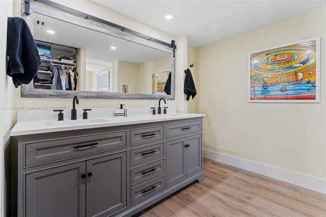 full bath featuring double vanity, wood finished floors, a sink, and baseboards