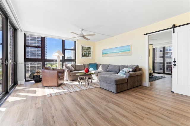 living room featuring a ceiling fan, a barn door, floor to ceiling windows, and wood finished floors