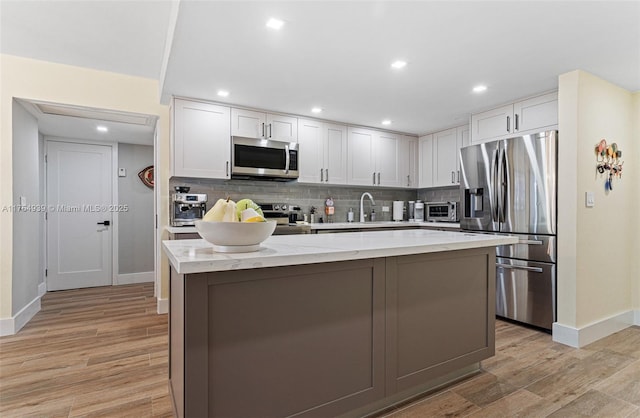 kitchen with appliances with stainless steel finishes, light wood-style floors, backsplash, and light stone counters