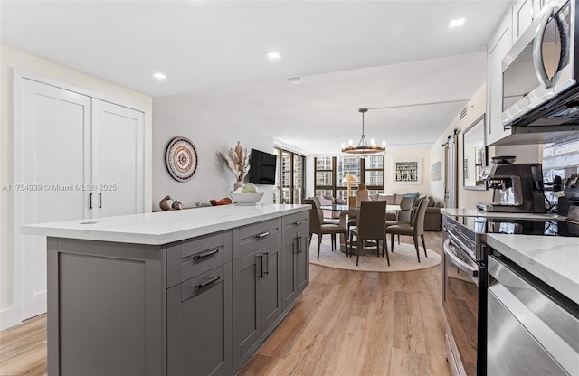 kitchen featuring stainless steel appliances, gray cabinets, a kitchen island, and light wood finished floors