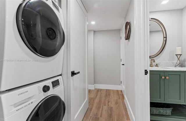 clothes washing area featuring laundry area, baseboards, stacked washer / dryer, light wood-style flooring, and a sink