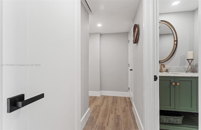 hallway featuring baseboards, a sink, and light wood finished floors