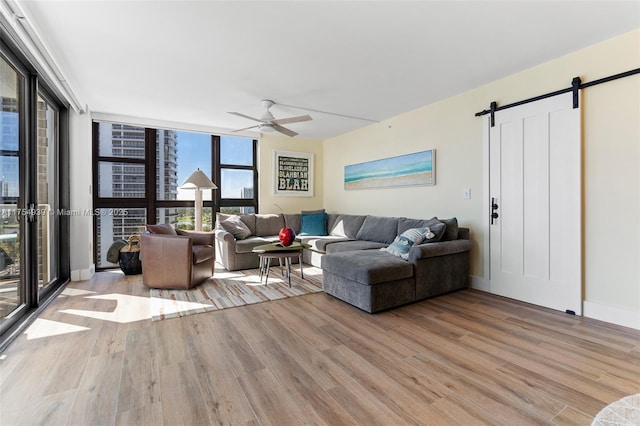 living area with a barn door, a ceiling fan, wood finished floors, a wall of windows, and baseboards