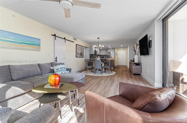 living area with light wood finished floors, a barn door, baseboards, and ceiling fan with notable chandelier