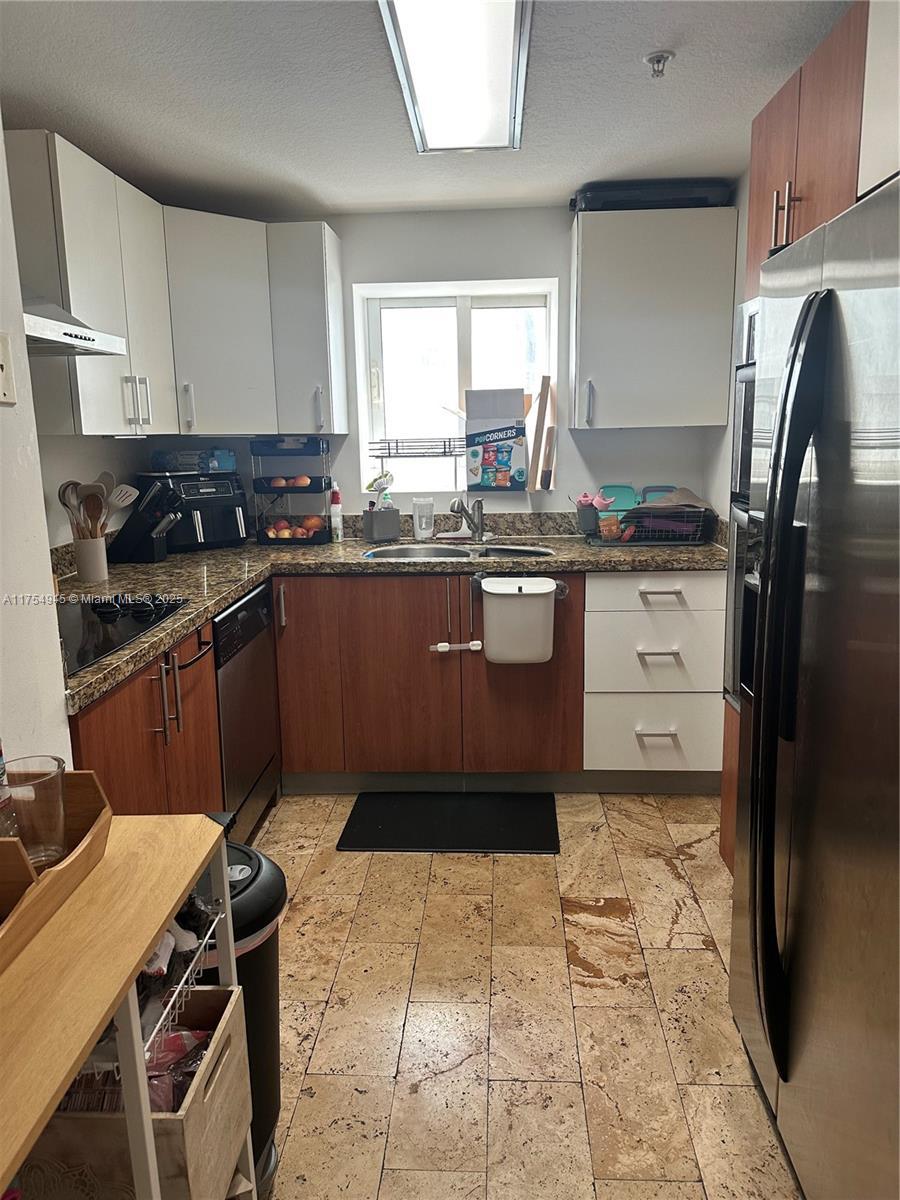 kitchen with white cabinetry, a sink, a textured ceiling, dark stone countertops, and black appliances