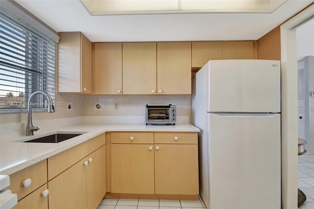 kitchen with a toaster, light brown cabinets, a sink, and freestanding refrigerator