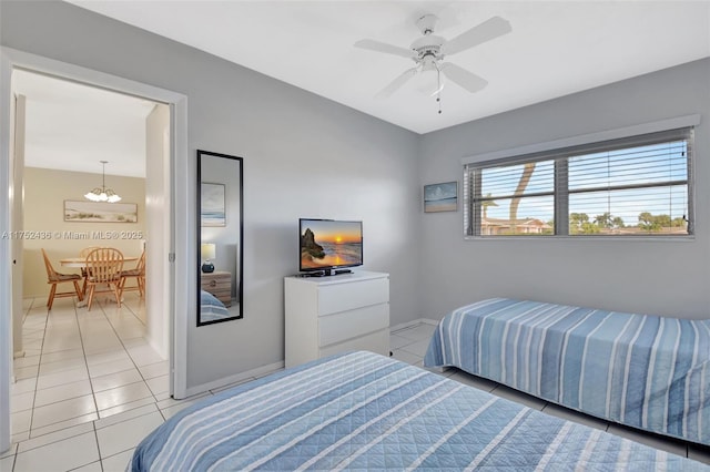 bedroom with ceiling fan with notable chandelier, baseboards, and light tile patterned floors