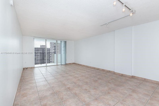 spare room featuring a textured ceiling, light tile patterned floors, expansive windows, and rail lighting