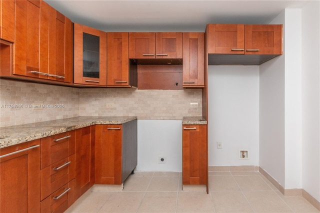 kitchen featuring brown cabinetry, light stone countertops, and light tile patterned floors