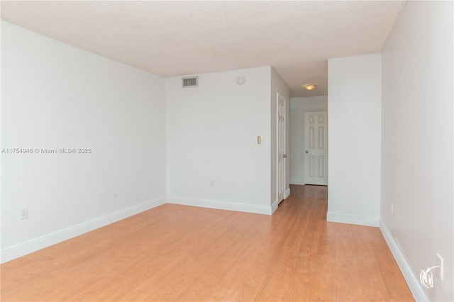 spare room featuring baseboards, visible vents, a textured ceiling, and light wood finished floors