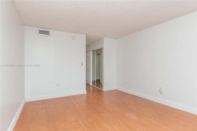 spare room with light wood finished floors, baseboards, visible vents, and a textured ceiling