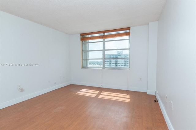 unfurnished room featuring light wood finished floors, baseboards, and a textured ceiling