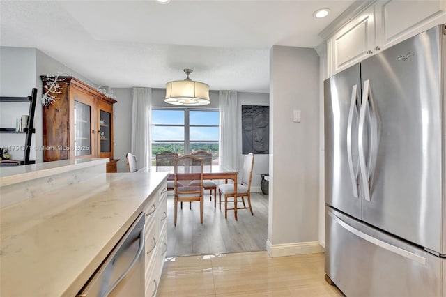 kitchen featuring stainless steel appliances, light wood-style floors, white cabinetry, light stone countertops, and baseboards