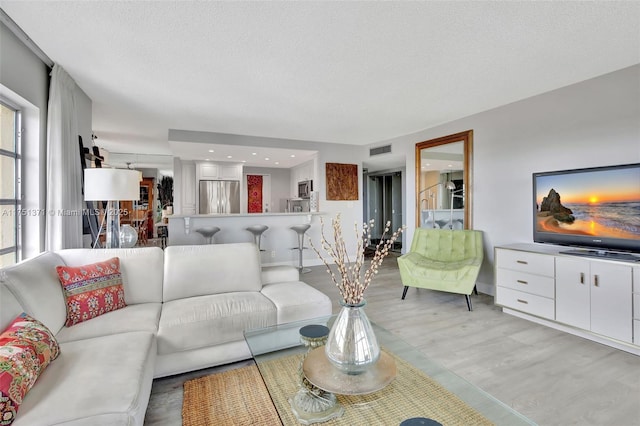 living room with a textured ceiling, visible vents, and light wood-style floors