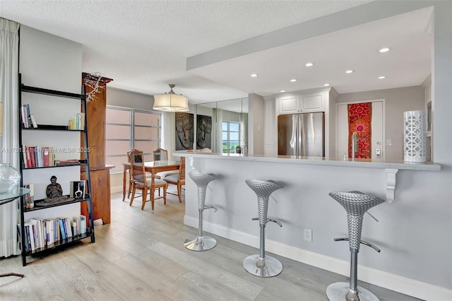 kitchen featuring freestanding refrigerator, a textured ceiling, light wood-type flooring, a kitchen bar, and white cabinetry