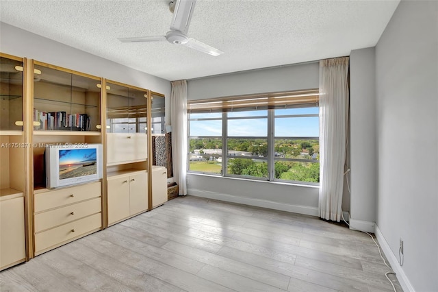 unfurnished bedroom featuring baseboards, ceiling fan, light wood-style flooring, and a textured ceiling