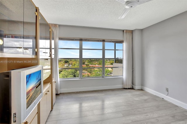 unfurnished room with light wood-style flooring, baseboards, and a textured ceiling