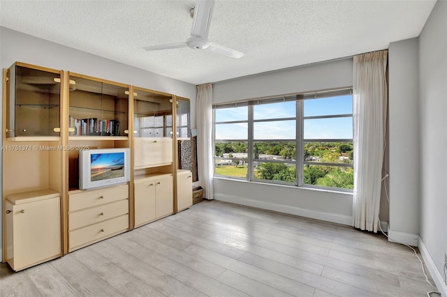 interior space featuring light wood-type flooring, ceiling fan, a textured ceiling, and baseboards