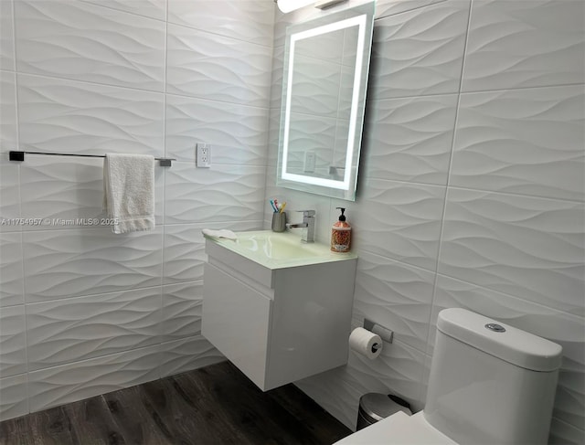 half bathroom featuring toilet, wood finished floors, tile walls, and vanity