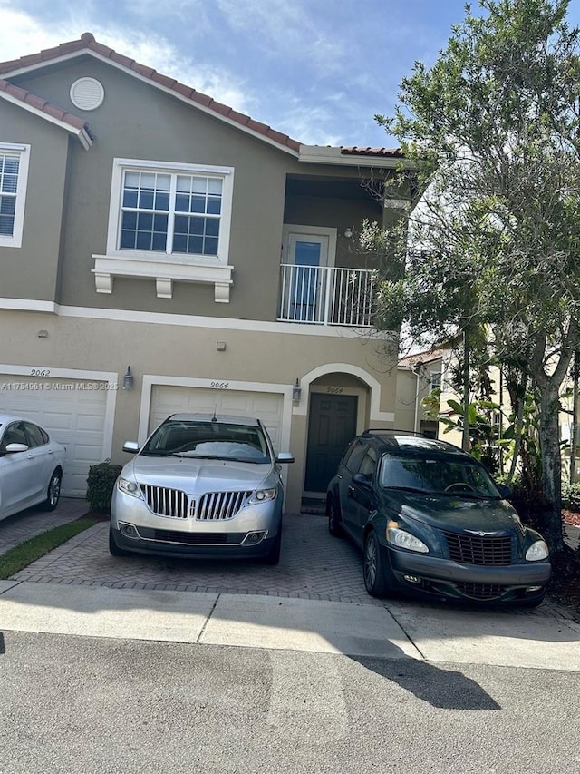 view of front of home featuring a tiled roof, an attached garage, a balcony, and stucco siding