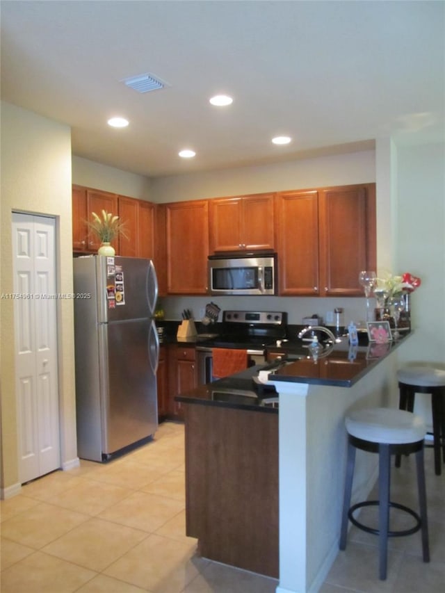 kitchen featuring a peninsula, visible vents, a kitchen breakfast bar, appliances with stainless steel finishes, and dark countertops