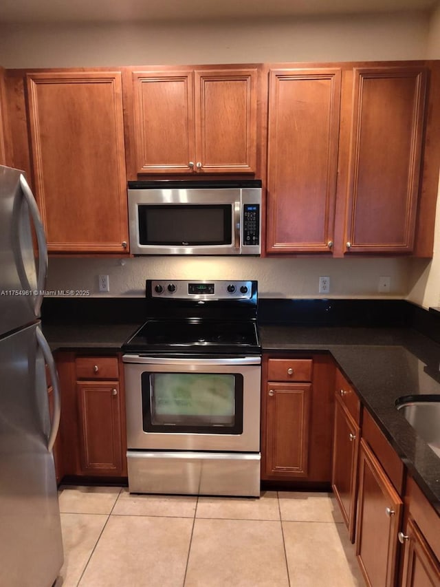 kitchen featuring brown cabinets, stainless steel appliances, dark stone countertops, and light tile patterned flooring