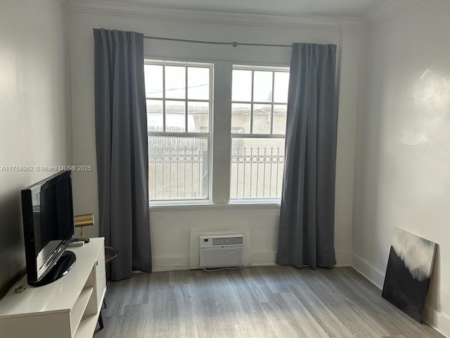 interior space with an AC wall unit, crown molding, baseboards, and wood finished floors