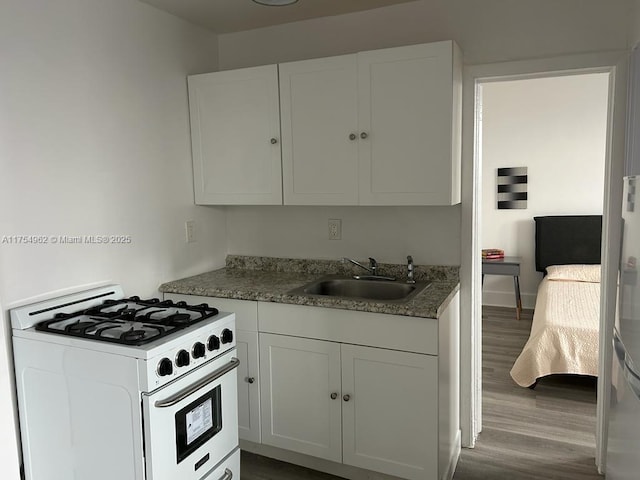 kitchen featuring white range with gas stovetop, white cabinetry, a sink, and wood finished floors